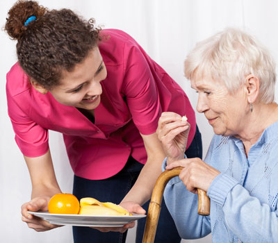 Care worker in a polo shirt helping an older woman with a meal